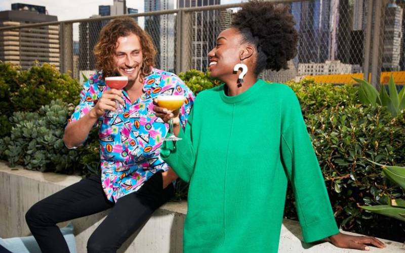 Image of man and woman enjoying drinks and laughing at Rooftop at QT Bar. 