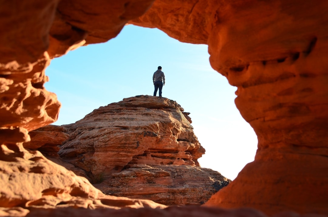 A man standing on a red rock butte, through a whole in the rick in St. George