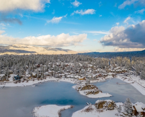 Aerial view of Big Bear Lake and town in California with the lake frozen on a sunny blue sky day in the Winter with pine trees below.